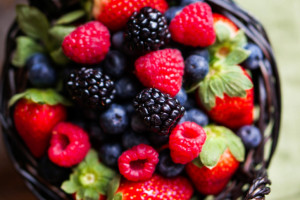 Mix of fresh berries in a basket on wooden background