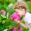 Beautiful blond little girl with long hair smelling flower
